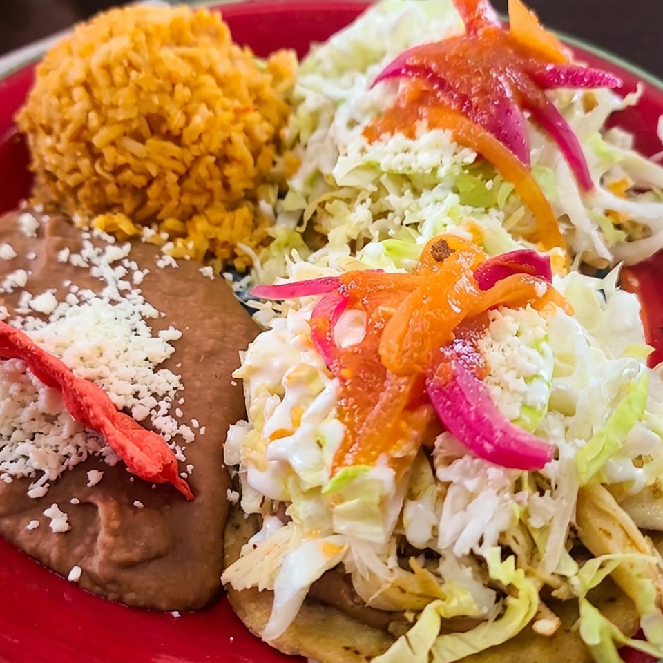 Mexican plate featuring refried beans, rice, salad, pickled vegetables, and a crispy tortilla on a red dish.